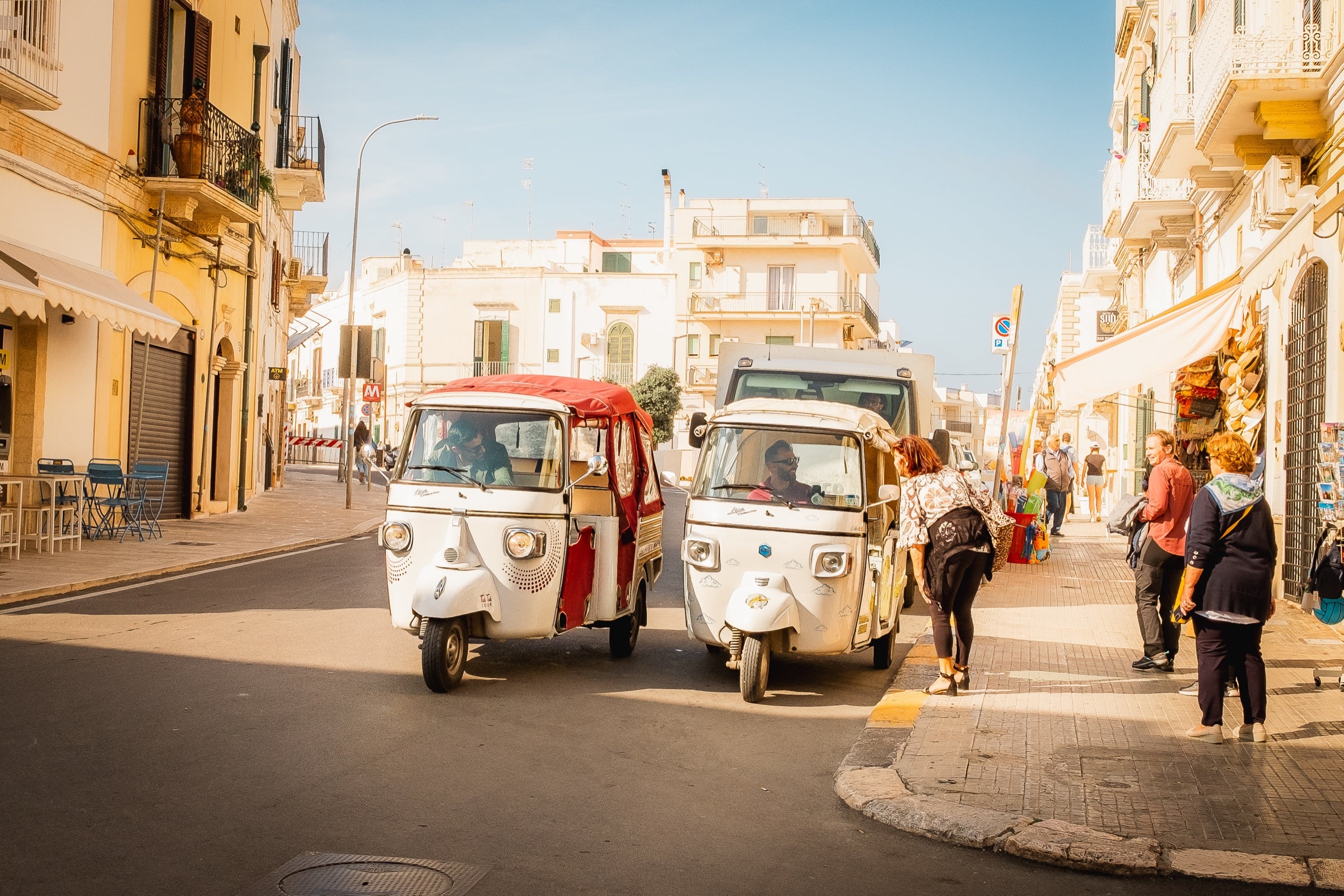 Two Piaggio Ape three-wheelers on a narrow Italian street